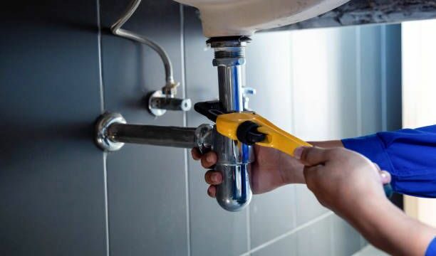 Plumber fixing white sink pipe with adjustable wrench.